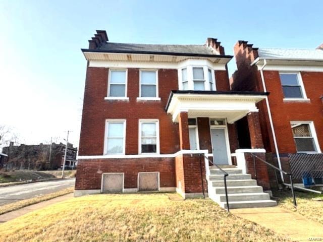 view of front of home featuring a chimney, a front lawn, a porch, and brick siding