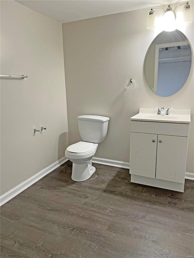 half bath featuring toilet, vanity, baseboards, and wood finished floors