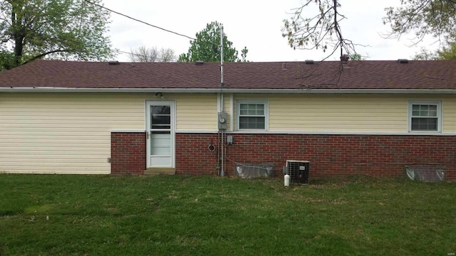 rear view of property with central AC, brick siding, a lawn, and roof with shingles