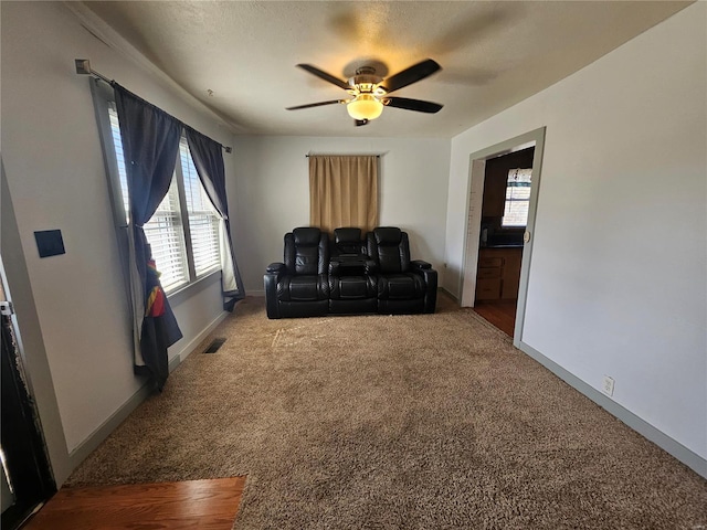 carpeted living room featuring baseboards, a textured ceiling, visible vents, and a ceiling fan