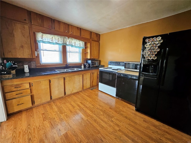 kitchen featuring light wood finished floors, brown cabinetry, dark countertops, black appliances, and a sink