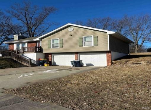 view of side of home with a garage, driveway, brick siding, and stairs