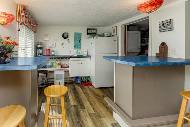 kitchen featuring dark wood finished floors, freestanding refrigerator, stacked washer and dryer, a textured ceiling, and dark countertops