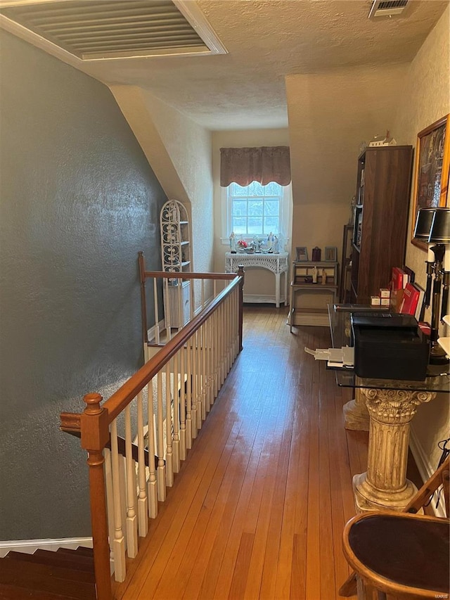 hall featuring visible vents, a textured wall, hardwood / wood-style flooring, a textured ceiling, and an upstairs landing