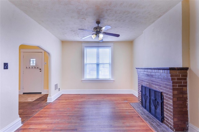 unfurnished living room with a brick fireplace, wood finished floors, arched walkways, and a textured ceiling