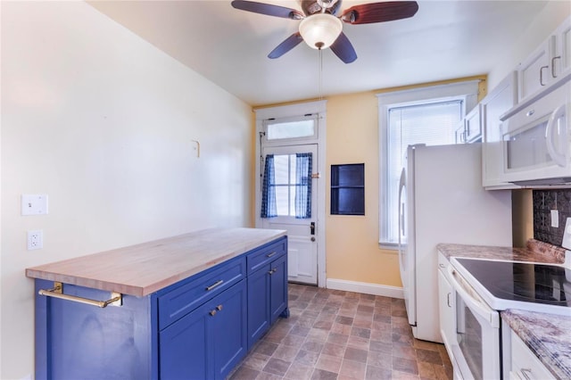 kitchen with white appliances, a ceiling fan, baseboards, blue cabinetry, and stone finish flooring