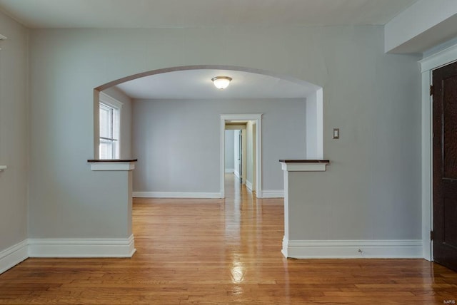 empty room featuring arched walkways, light wood-style flooring, and baseboards