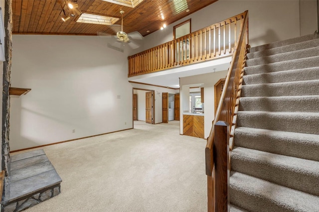stairs with ceiling fan, a skylight, wooden ceiling, high vaulted ceiling, and carpet