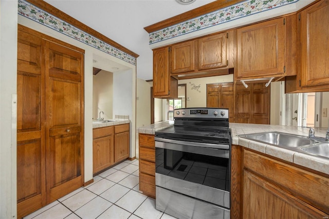 kitchen featuring stainless steel electric range oven, a sink, tile counters, brown cabinetry, and light tile patterned floors
