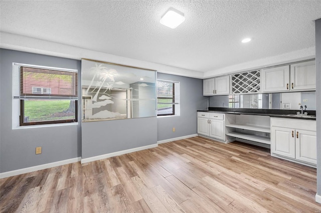 kitchen with a textured ceiling, dark countertops, open shelves, a sink, and light wood finished floors