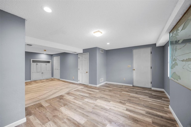 finished basement with light wood-type flooring, a textured ceiling, baseboards, and visible vents