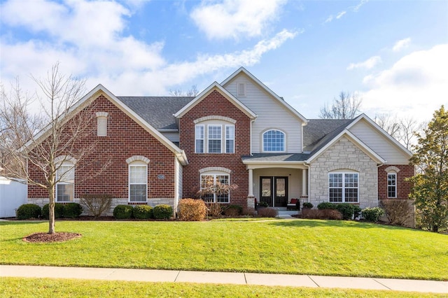 traditional home with brick siding, a shingled roof, stone siding, and a front yard