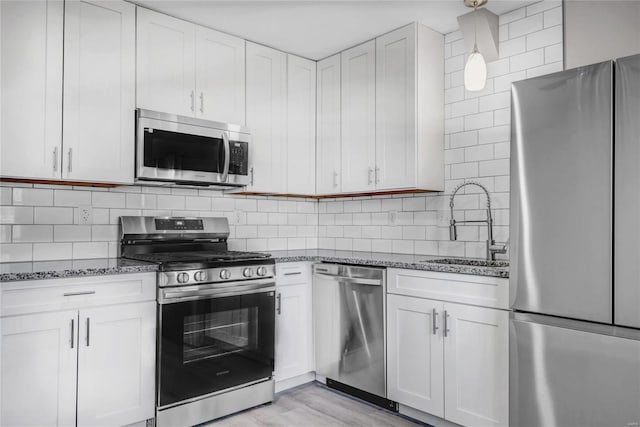 kitchen featuring a sink, dark stone counters, backsplash, and appliances with stainless steel finishes