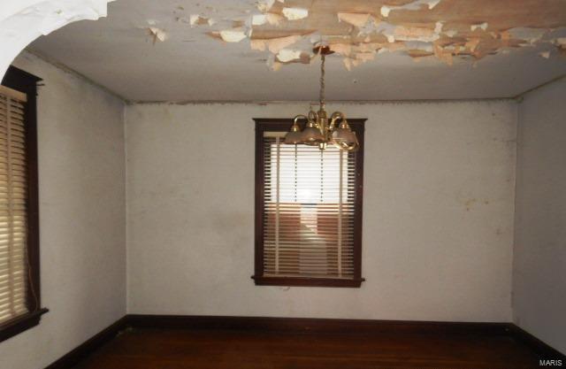 unfurnished room featuring an inviting chandelier, baseboards, and wood finished floors