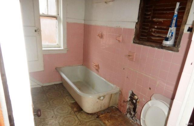 bathroom featuring a tub to relax in, tile walls, and toilet