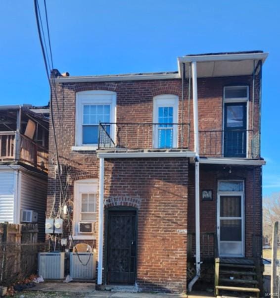 view of front of home with entry steps, brick siding, fence, and a balcony