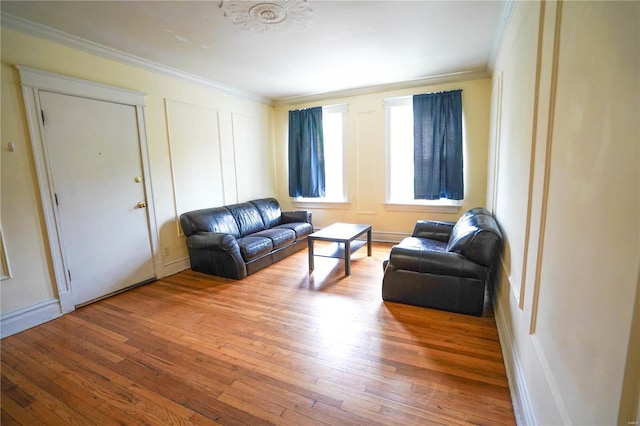 living area with crown molding, a decorative wall, and hardwood / wood-style floors