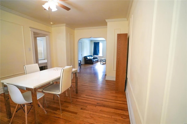 dining area featuring ceiling fan, arched walkways, wood finished floors, and ornamental molding