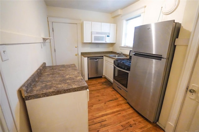 kitchen with light wood-style flooring, stainless steel appliances, a sink, white cabinetry, and dark countertops