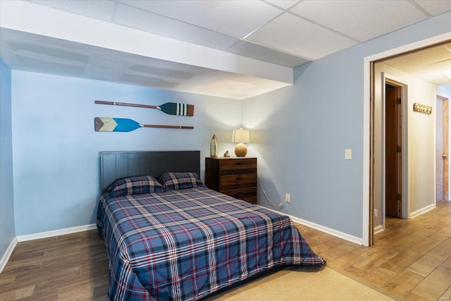 bedroom with wood finished floors, baseboards, and a drop ceiling