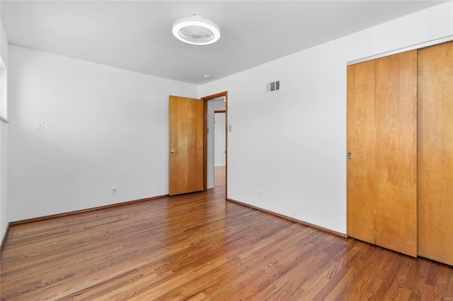 unfurnished bedroom with a closet, visible vents, baseboards, and wood finished floors