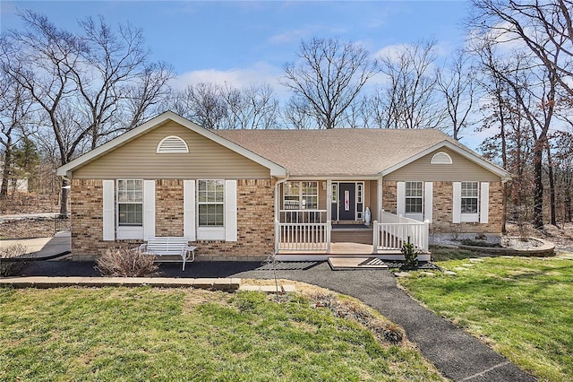 single story home featuring a front yard, brick siding, roof with shingles, and a wooden deck