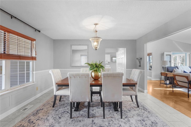 dining area featuring visible vents, a wainscoted wall, a textured ceiling, light wood-style floors, and a decorative wall