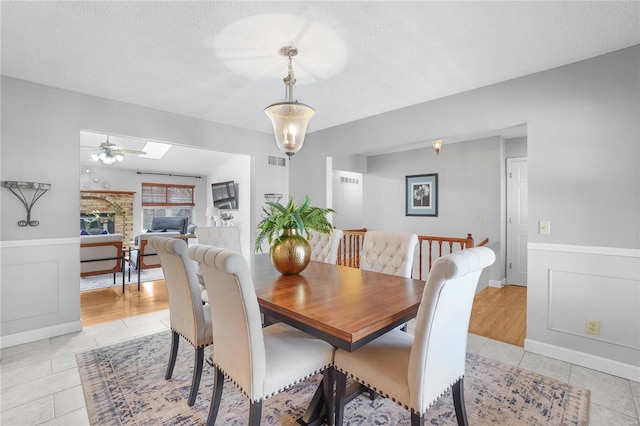 dining space featuring visible vents, light tile patterned floors, a fireplace, a textured ceiling, and a ceiling fan