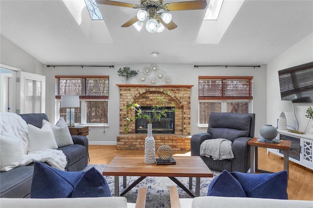 living area featuring baseboards, vaulted ceiling with skylight, a brick fireplace, and wood finished floors