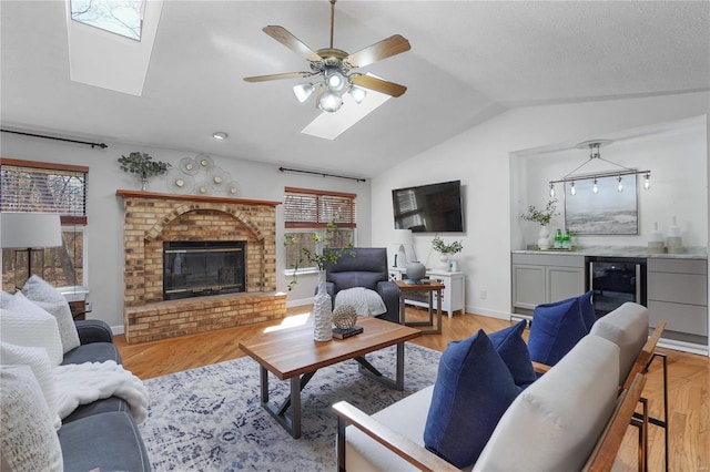 living room with wine cooler, light wood-style floors, a fireplace, lofted ceiling, and ceiling fan