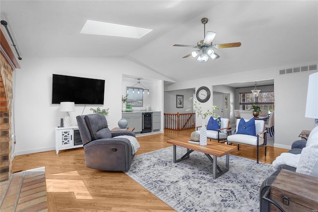 living room with visible vents, wine cooler, lofted ceiling with skylight, light wood-type flooring, and a ceiling fan