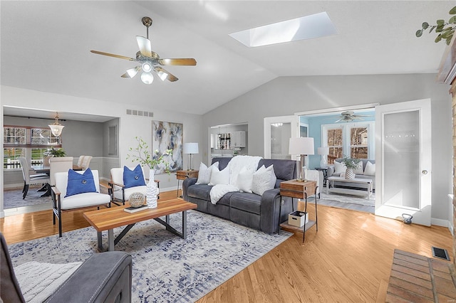 living area featuring vaulted ceiling with skylight, light wood-style flooring, and visible vents