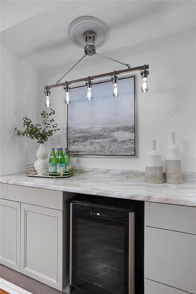 bar featuring wine cooler, a textured ceiling, and a bar