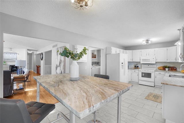 kitchen with washer and clothes dryer, a sink, tasteful backsplash, white appliances, and white cabinets