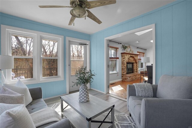 living area featuring baseboards, light wood-style floors, a brick fireplace, and ceiling fan