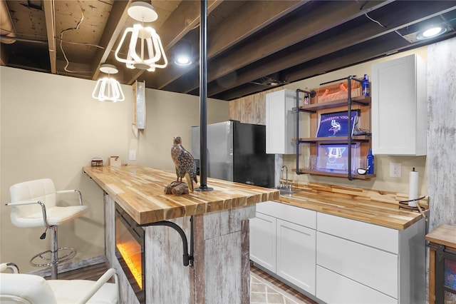 kitchen featuring a sink, wooden counters, white cabinetry, and freestanding refrigerator