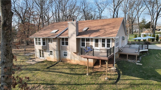 rear view of house with a wooden deck, a chimney, a yard, and roof with shingles