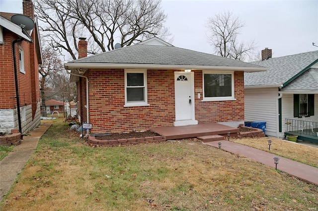 bungalow featuring a shingled roof, a front yard, brick siding, and a chimney