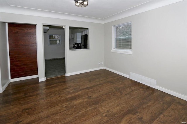 spare room featuring dark wood-style flooring, visible vents, and baseboards