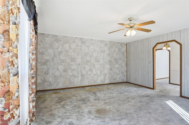 carpeted empty room with baseboards, arched walkways, and a ceiling fan