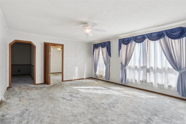 carpeted empty room featuring baseboards, a ceiling fan, arched walkways, and a textured ceiling