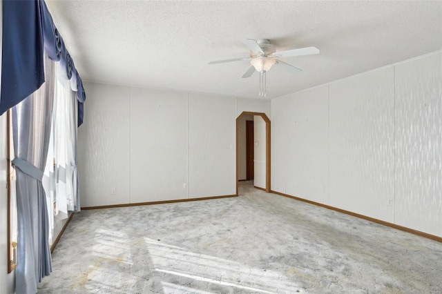 spare room with arched walkways, a textured ceiling, carpet floors, and ceiling fan