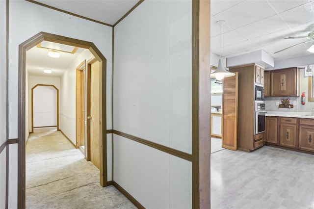 corridor featuring arched walkways, light wood-type flooring, baseboards, and a sink