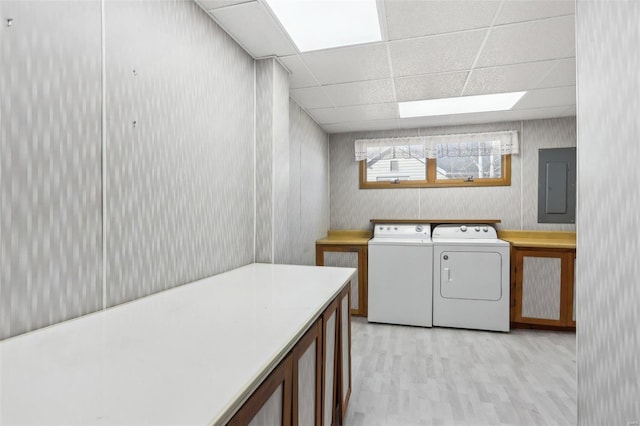 laundry room with electric panel, light wood-type flooring, cabinet space, and washing machine and dryer