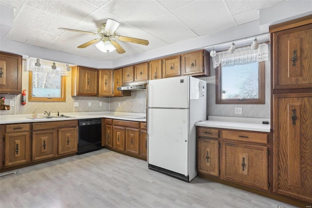 kitchen featuring freestanding refrigerator, a sink, under cabinet range hood, dishwasher, and brown cabinets