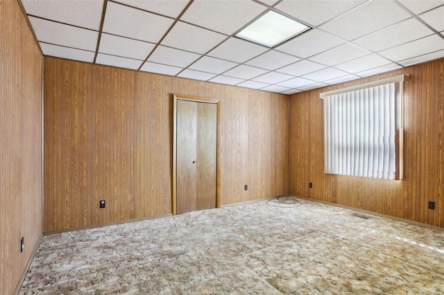 carpeted spare room with visible vents, wood walls, and a paneled ceiling