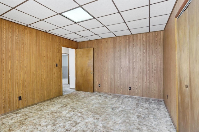 carpeted empty room with wooden walls and a paneled ceiling