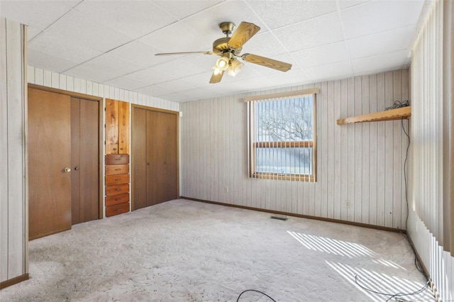 unfurnished bedroom with baseboards, visible vents, ceiling fan, carpet flooring, and two closets