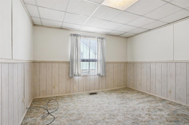 carpeted spare room featuring wooden walls, a drop ceiling, wainscoting, and visible vents