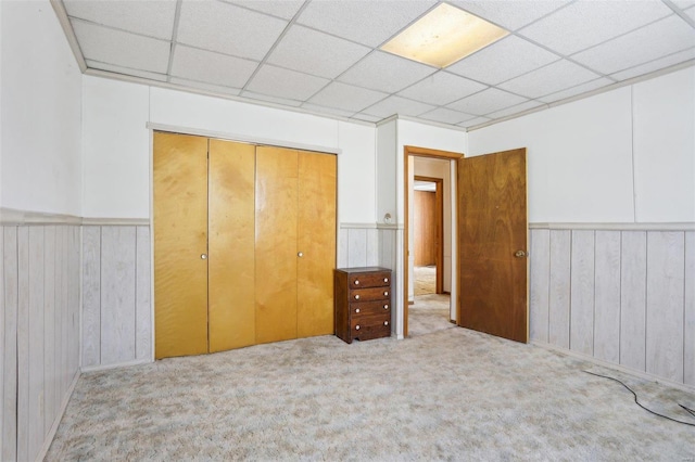 unfurnished bedroom with a drop ceiling, carpet, a closet, and a wainscoted wall